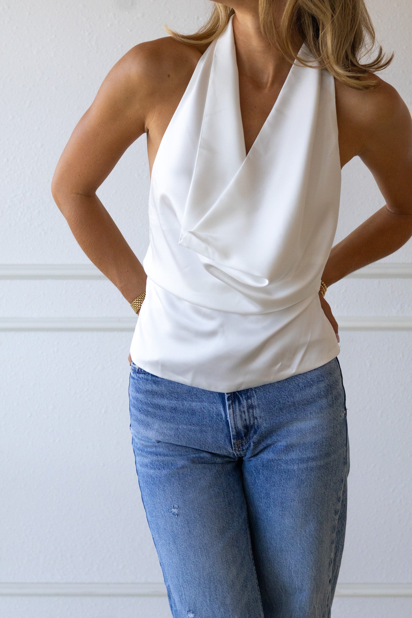 Woman wearing a white halter top and blue jeans against a plain background