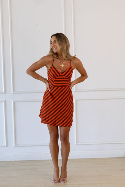 Woman wearing a red and black striped dress against a white paneled wall.