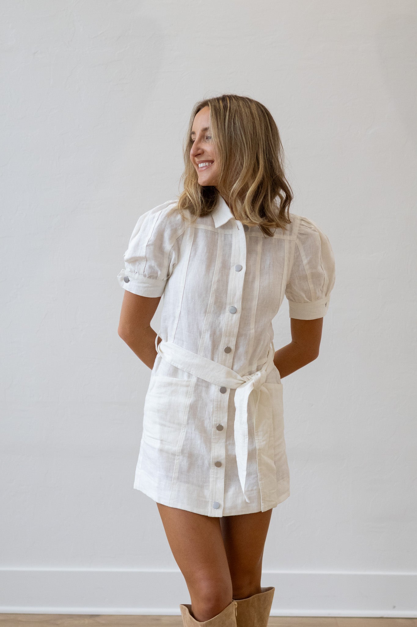Woman wearing a white striped dress with a belt against a plain background