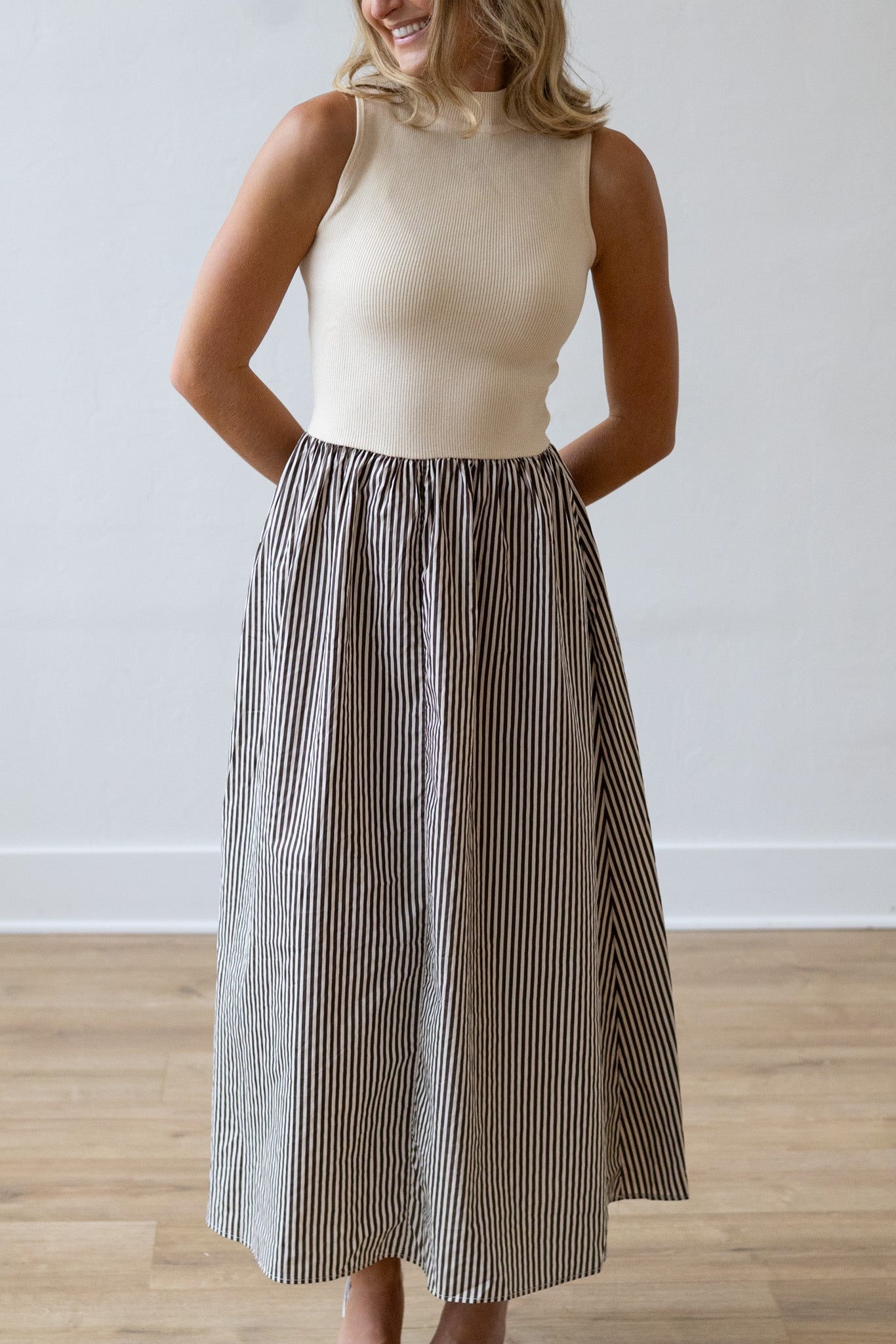 Woman wearing a beige sleeveless top and striped skirt on a plain background