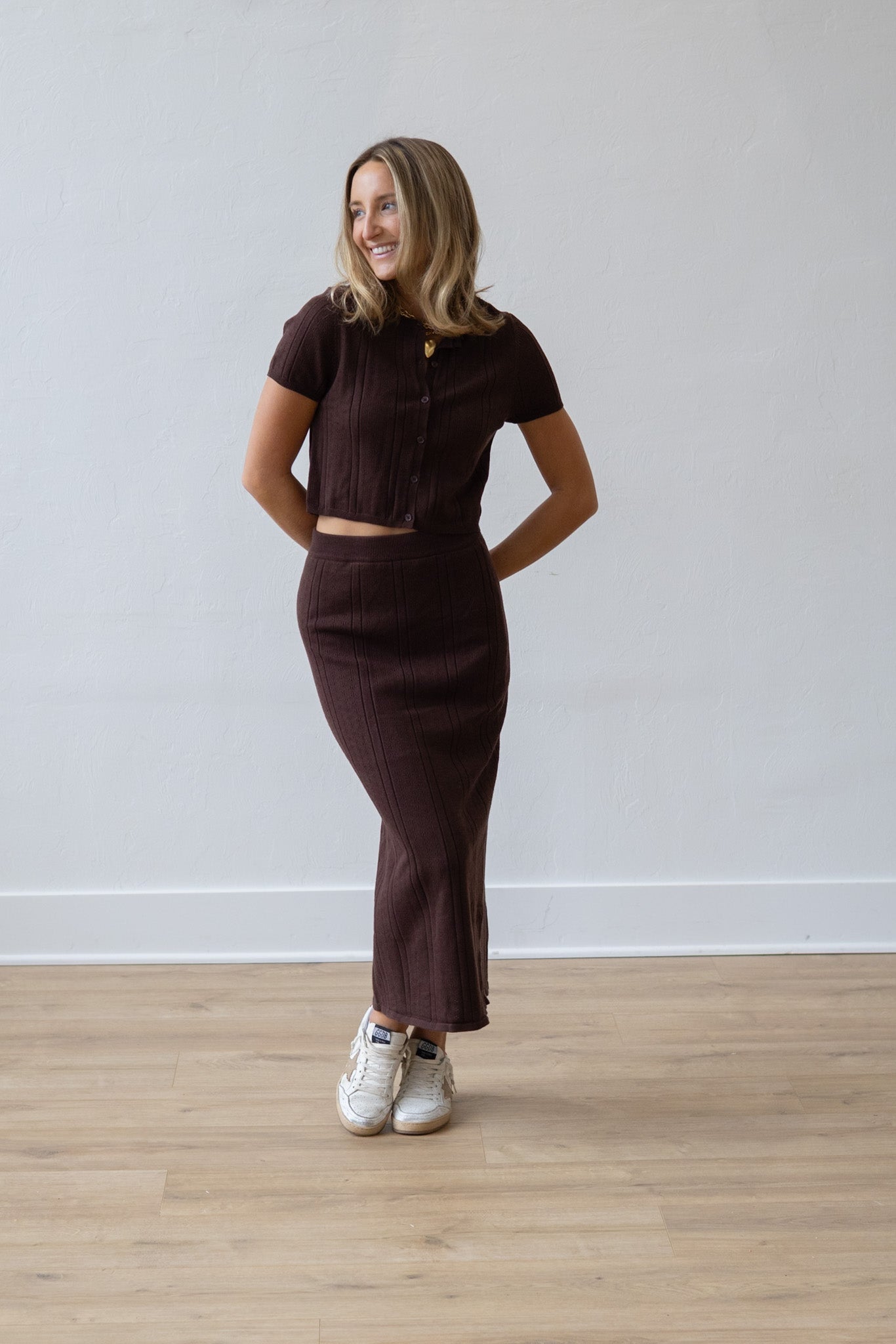 Woman wearing a brown outfit standing against a plain white wall.