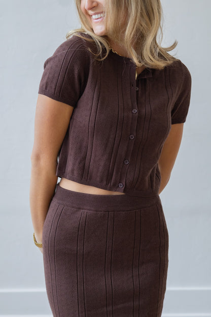 Woman wearing a brown outfit with a matching top and skirt against a plain background