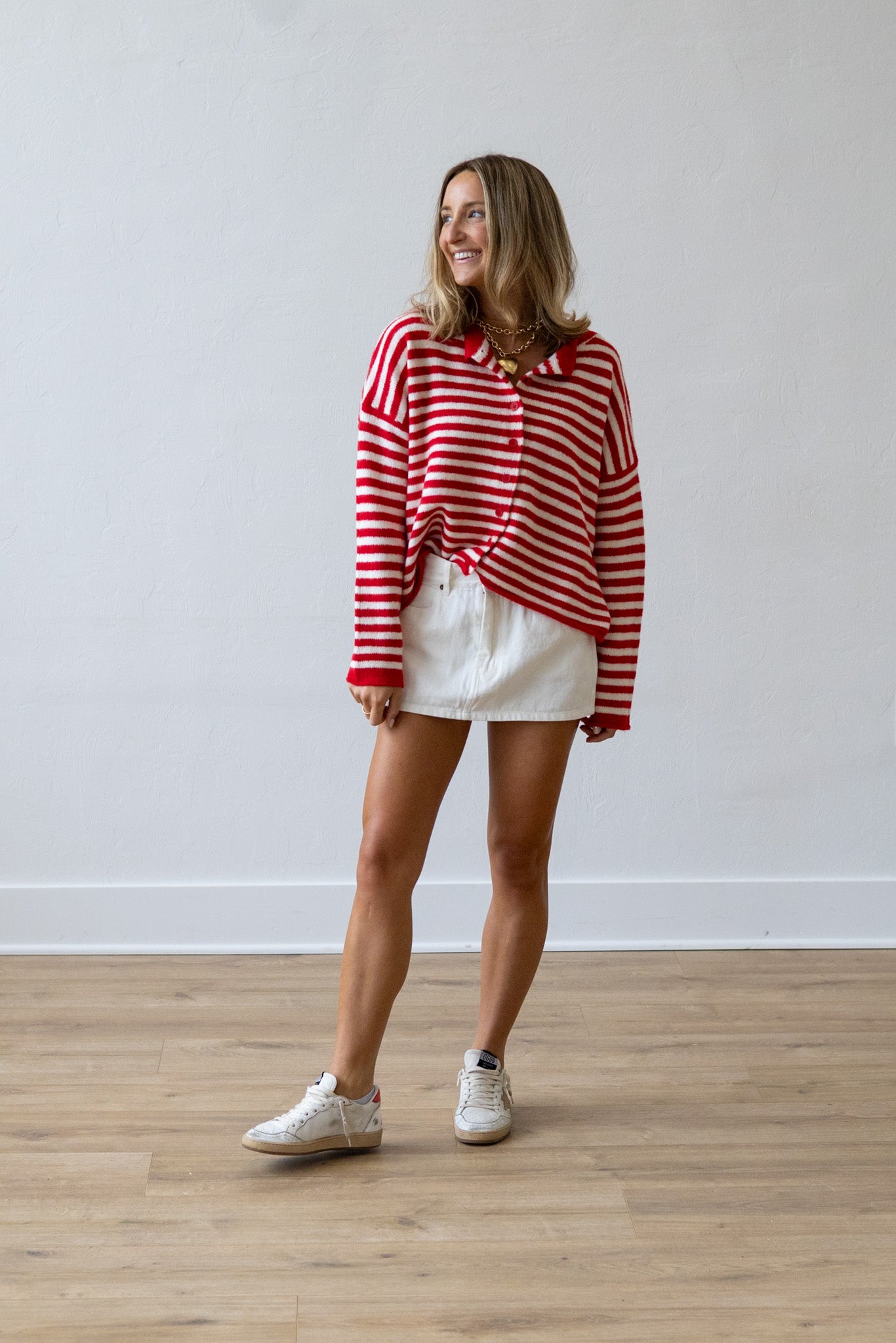 Woman wearing a red and white striped shirt and white shorts standing on a wooden floor.