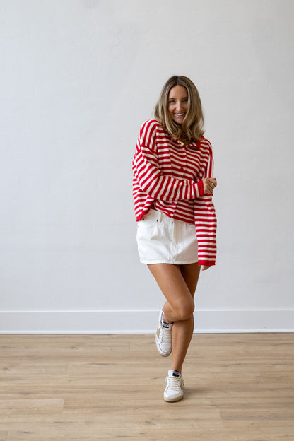 Woman wearing a red and white striped sweater and white shorts standing on a wooden floor.