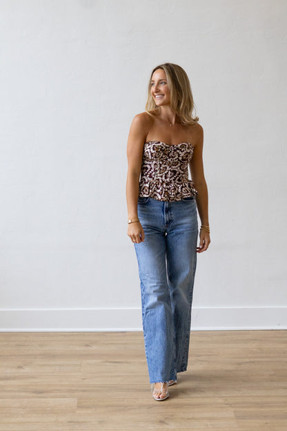 Woman wearing a patterned top and blue jeans standing against a white wall.