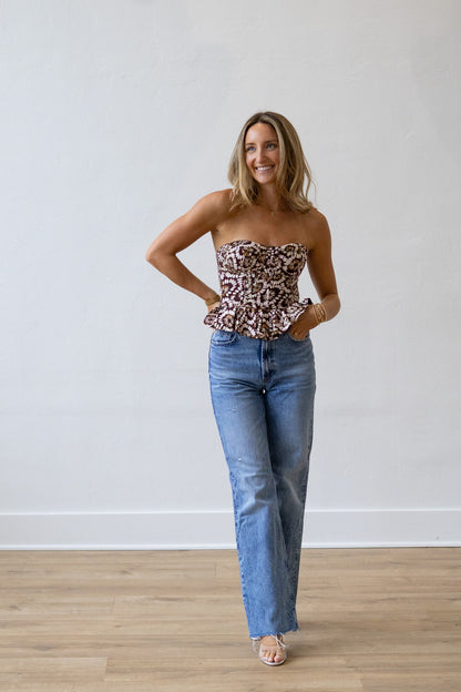 Woman wearing a floral print top and blue jeans against a white wall.