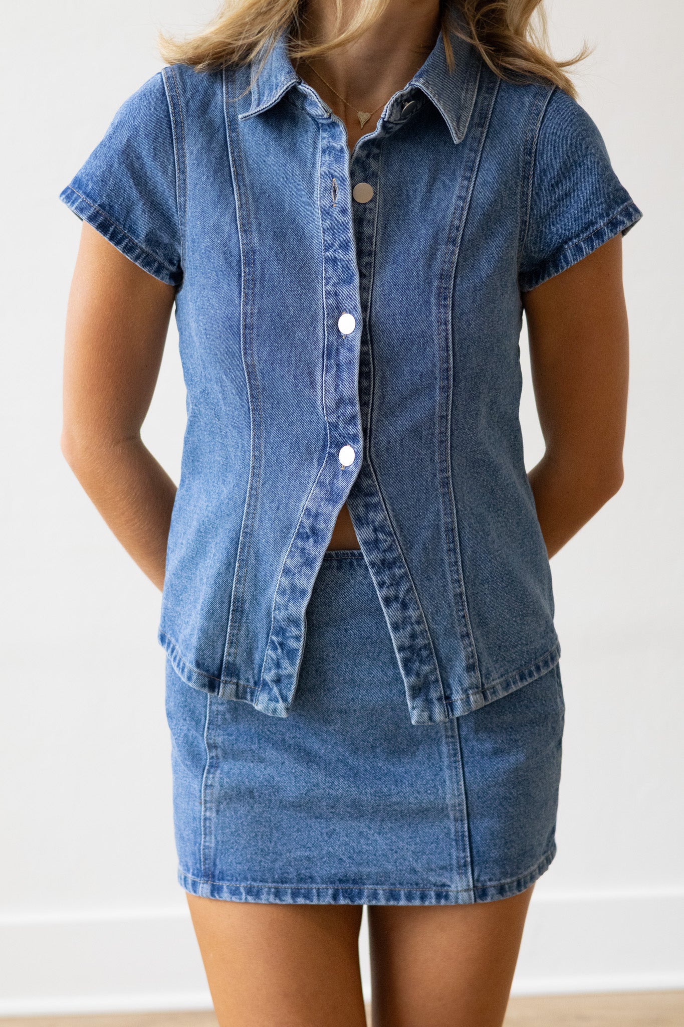 Person wearing a denim shirt and skirt set against a white background