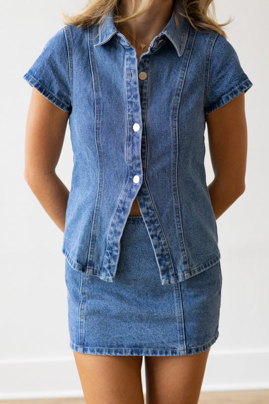 Person wearing a denim shirt and skirt set against a white background