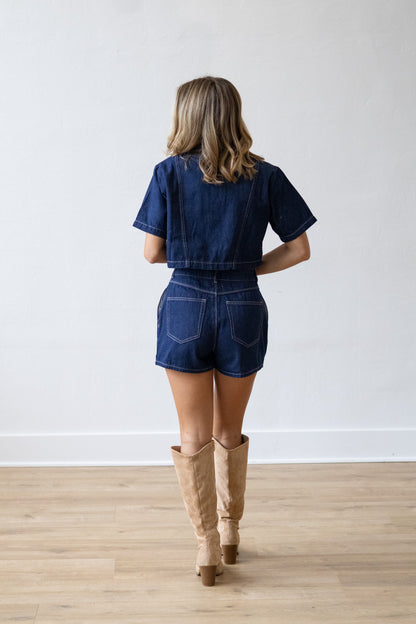 Person wearing a denim outfit with knee-high boots on a plain background