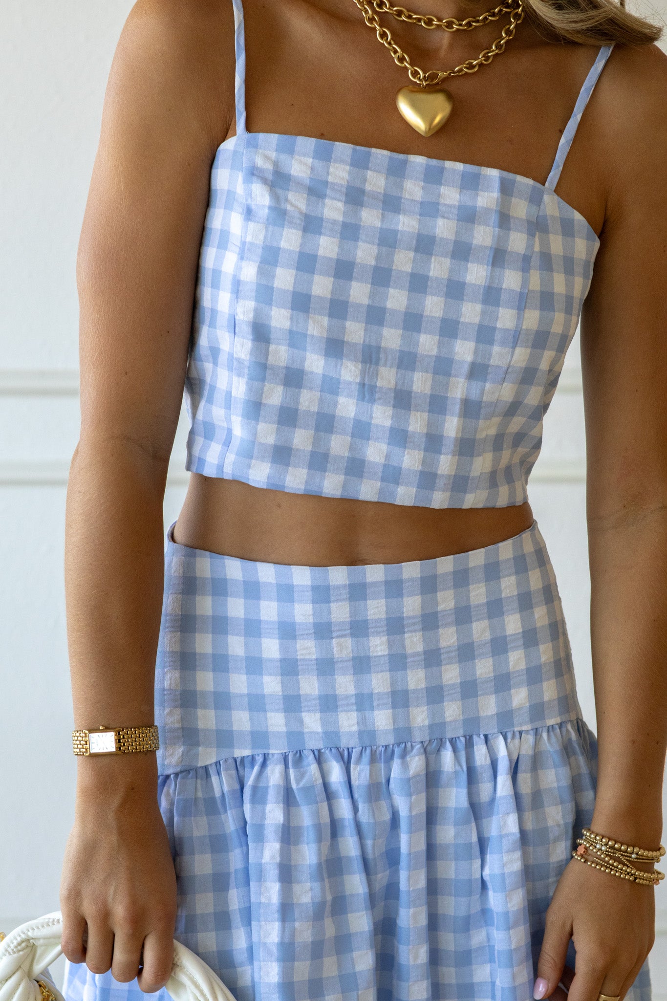 Person wearing a blue and white checkered dress with gold jewelry against a neutral background
