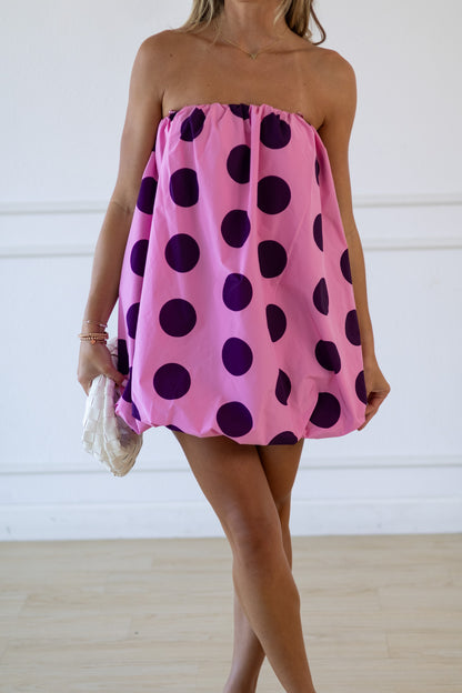 Woman wearing a pink strapless dress with purple polka dots against a white background