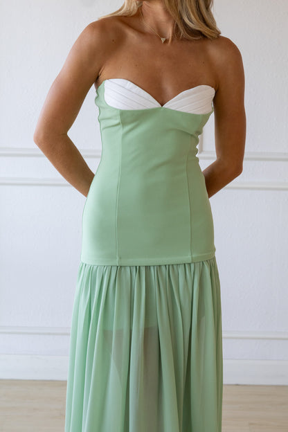 Woman wearing a strapless green dress with a white top against a plain background