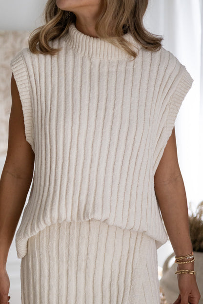 Person wearing a beige ribbed sleeveless top and skirt set with a blurred background