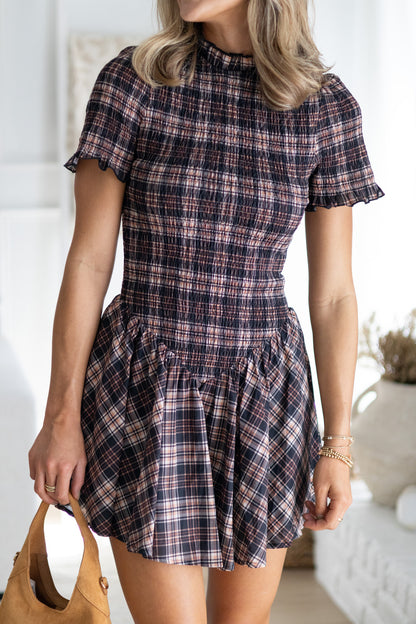 Woman wearing a plaid dress holding a brown bag indoors.